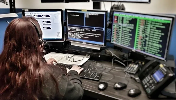 A woman sitting at her computer desk with three monitors.